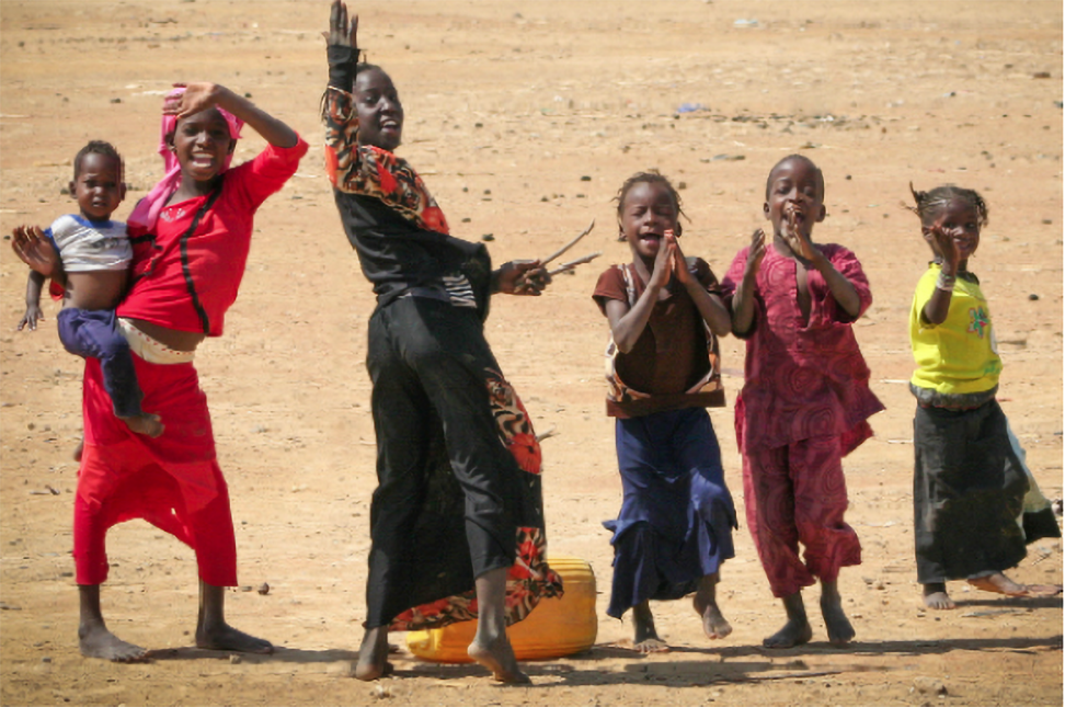 Two African women dance with four children